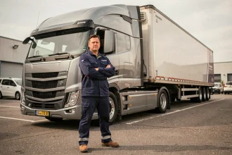 Chauffeur professionnel de poids lourd debout devant un camion semi-remorque dans un dépôt logistique, illustrant le permis C pour la conduite professionnelle