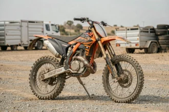 Moto cross non homologuée garée dans un paddock de circuit avec boue sur les fourches et absence de rétroviseurs